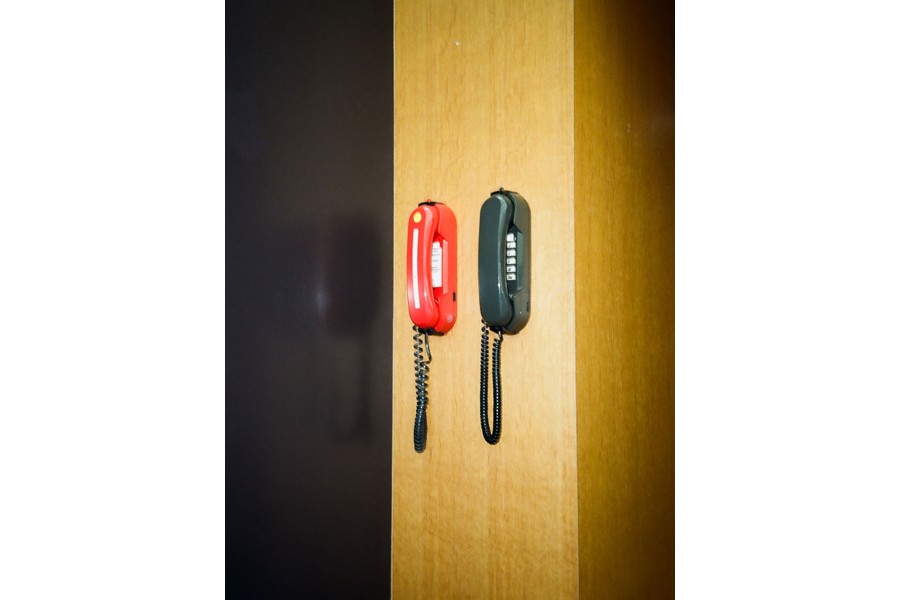 Zwei verschiedenfärbige hängende Tastentelefone an einer Holzwand nebeneinander